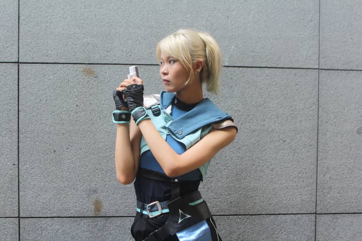 Young woman in futuristic cosplay outfit holding a blaster, posing against a neutral background.