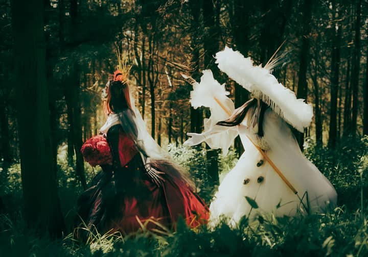 Two people in elaborate costumes explore an enchanting forest setting, creating a whimsical fairytale atmosphere.