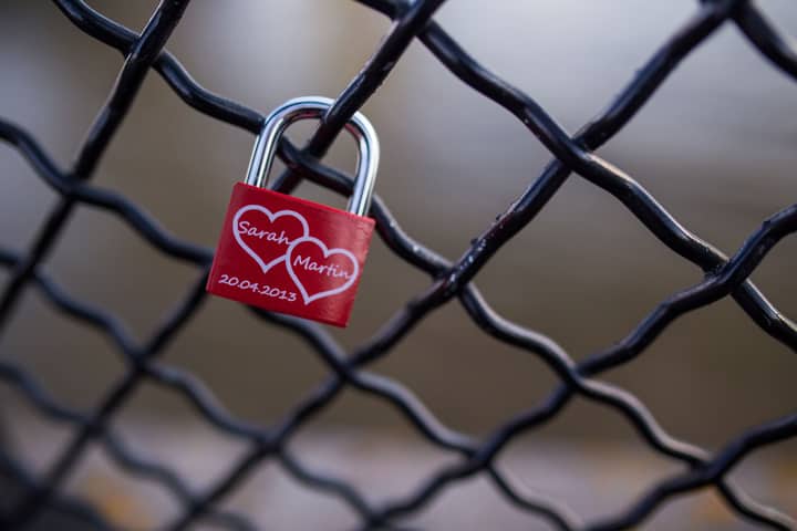 A red love padlock with names on a chain link fence, symbolizing eternal love.