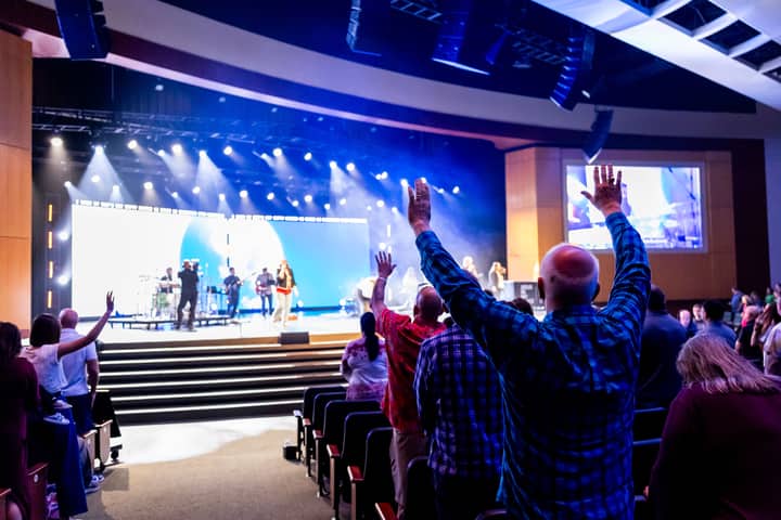 A lively worship service with an audience raising hands to a live band on stage in a church.