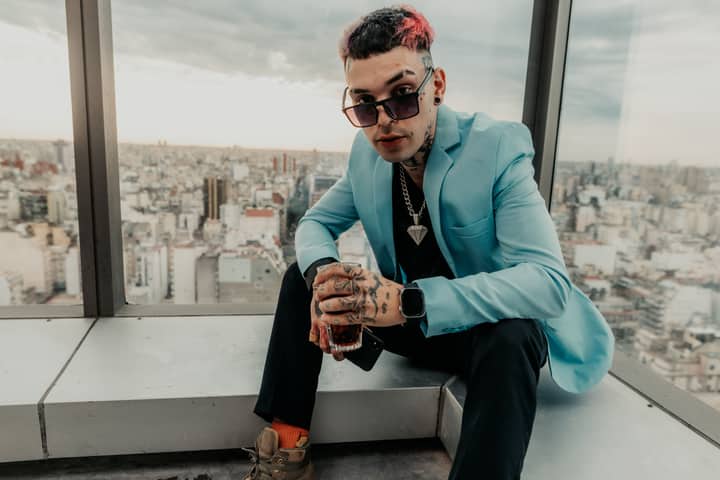 Stylish man with tattoos enjoys a drink on a Buenos Aires skyscraper rooftop, cityscape background.