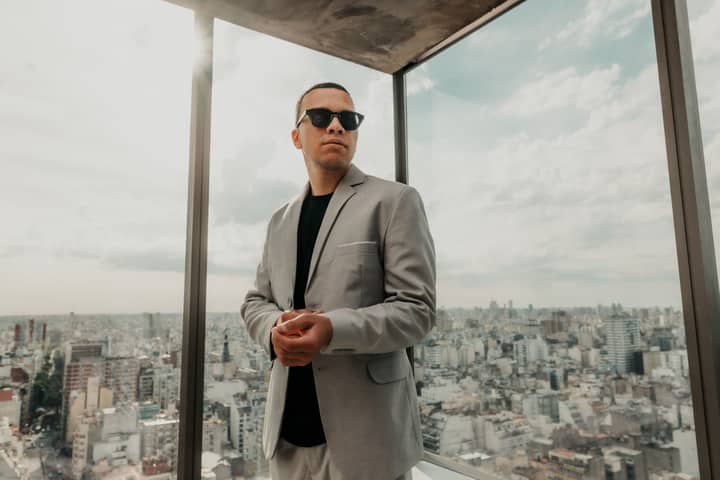 Confident man in a suit with sunglasses overlooking Buenos Aires cityscape from a modern office building.