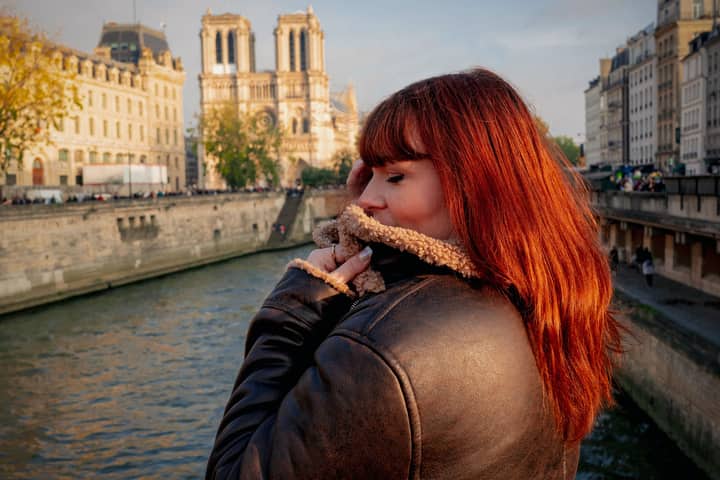 Woman in autumn attire by the Seine with Notre Dame in the background, capturing Parisian style.
