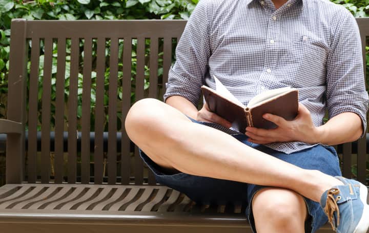 A man relaxing and reading a book on a bench outdoors, enjoying a leisurely afternoon.