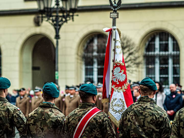 Polish soldiers in uniform during a ceremonial parade with national flag.