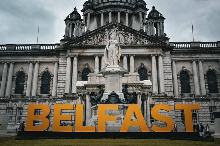 View of the Belfast City Hall with striking statue and Belfast sign, showcasing historical architecture.