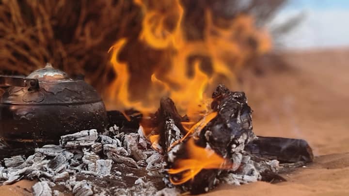 A rustic kettle by a campfire in the Algerian desert, capturing a traditional tea brewing session.
