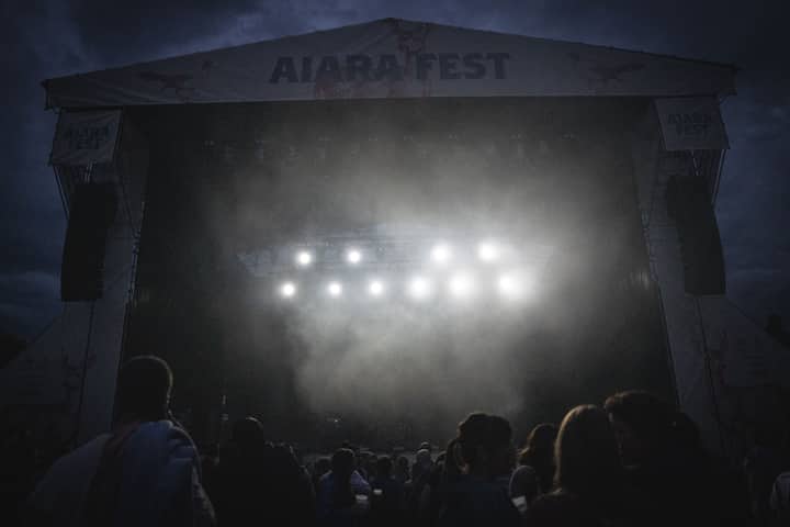 A misty night music festival scene with bright stage lights and a crowd of people.