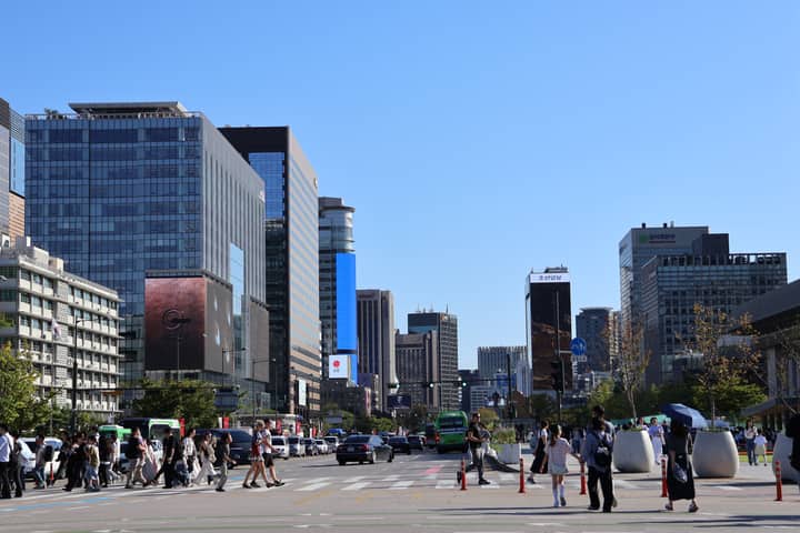 Vibrant street scene in Seoul with skyscrapers and people crossing under a clear blue sky.