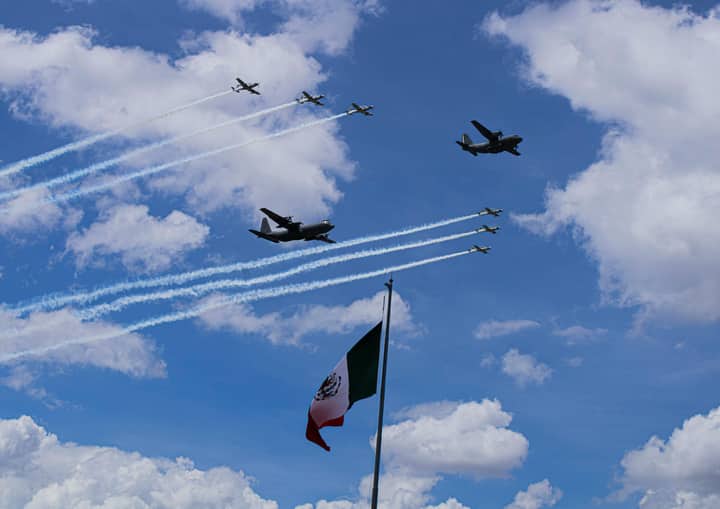 Dynamic military airshow with jets and smoke trails above a Mexican flag.