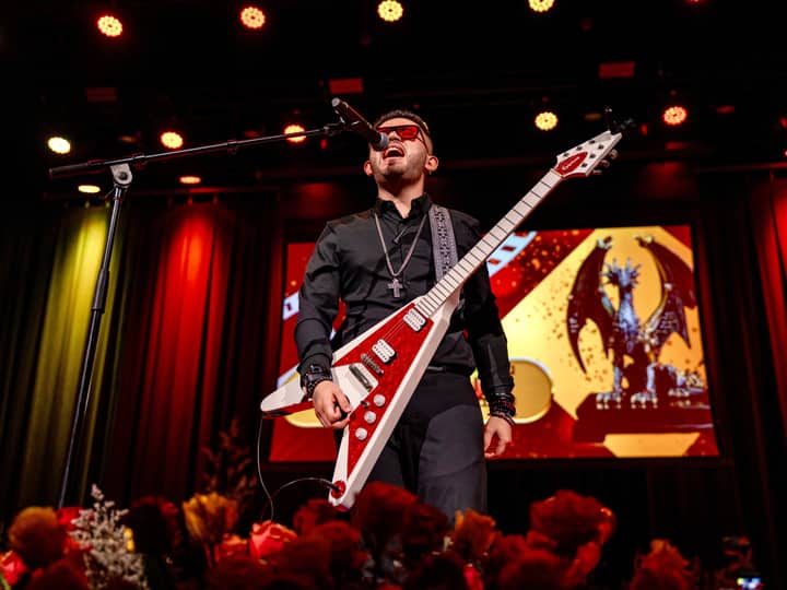Energetic rock musician performing on stage with electric guitar and microphone under vibrant lights.