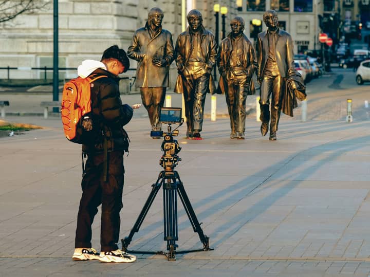 A photographer with a tripod captures the famous Beatles statues in Liverpool, England.
