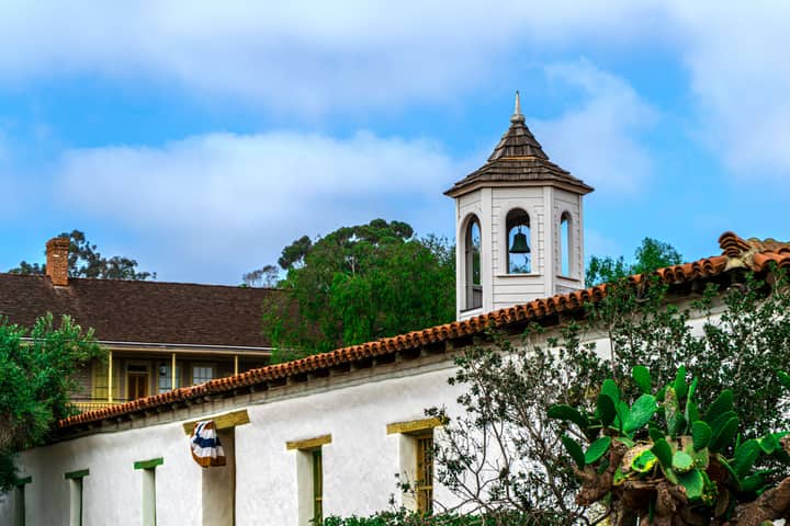 A picturesque view of a historic mission bell tower surrounded by lush greenery in San Diego, CA.