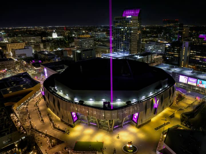 Aerial view of Golden 1 Center in downtown Sacramento illuminated at night with vibrant purple lights.