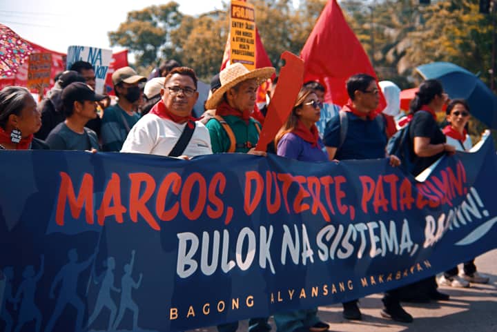 A group of protesters holding a banner during a daytime demonstration outdoors.