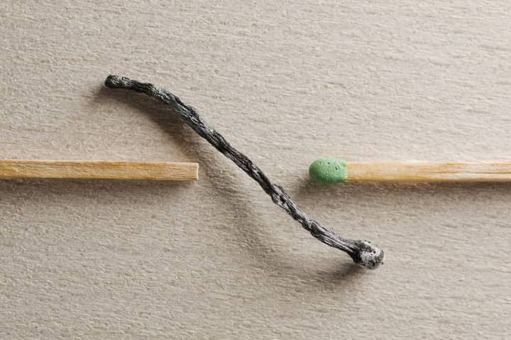 Artistic depiction of contrast between a burnt and unused match on a textured surface.