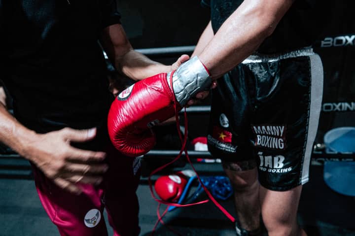 Boxer getting ready for a fight with trainer's help, showcasing red gloves and black shorts.