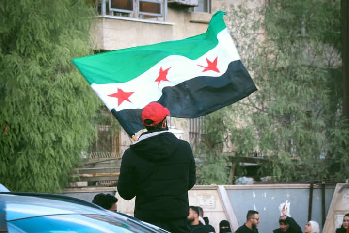 Group of people waving the Syrian flag at a demonstration, showcasing patriotism and unity.
