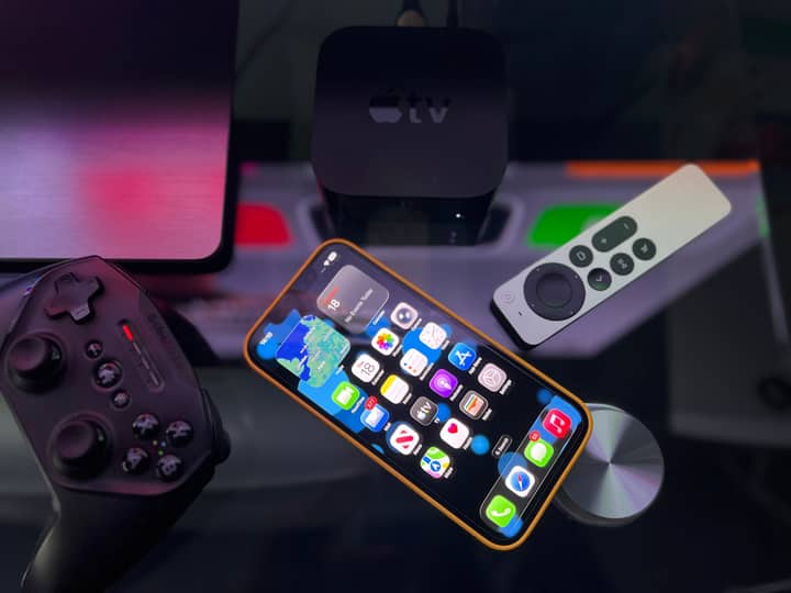 Stylish home entertainment setup featuring an iPhone, Apple TV, and gaming controller on a dark surface.