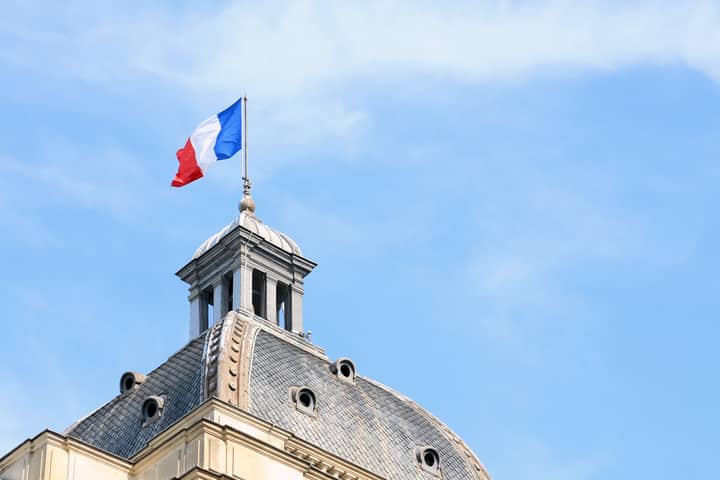The French flag waves atop the dome of historic architecture in Paris, France.