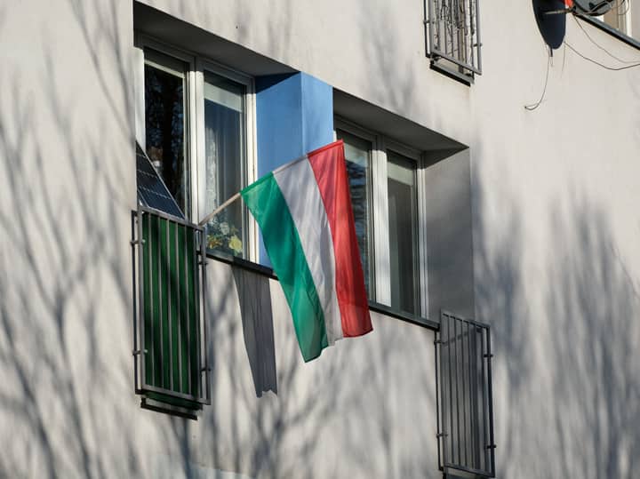 Hungarian flag hanging from a window on an urban apartment building, casting soft shadows.