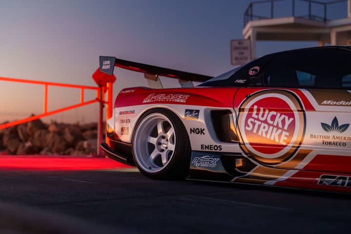 Dynamic sunset view of a sportscar adorned with racing decals on a coastal road.