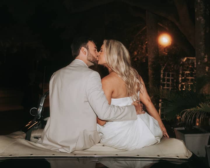 Newlywed couple sharing a romantic kiss seated on a classic car at night.