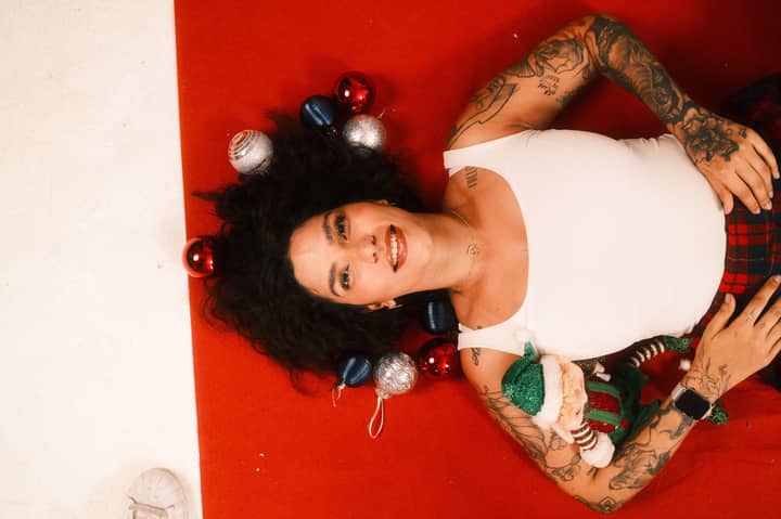 A joyful woman lying on a red surface surrounded by Christmas ornaments, exuding a festive holiday spirit.