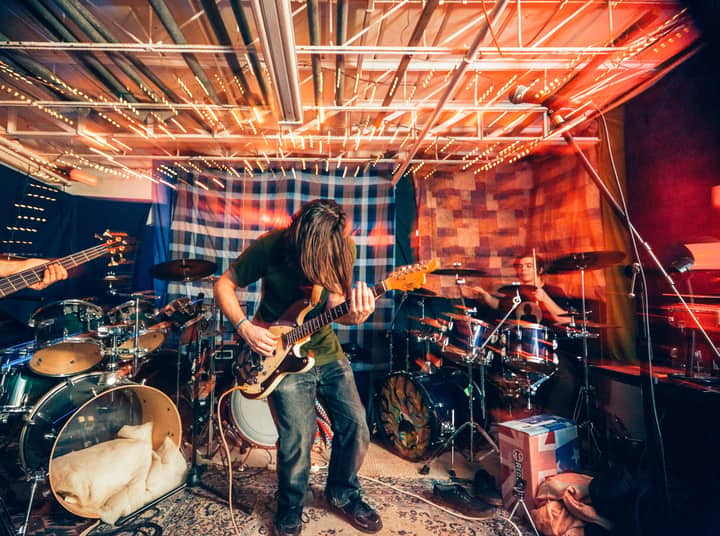 Energetic rock band performance with electric guitar and drums under colorful lights indoors.