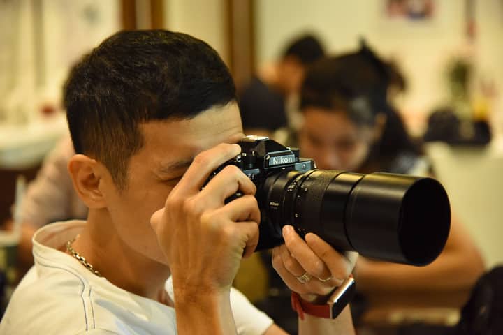 Male photographer using a Nikon camera indoors with blurred background.