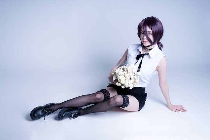 Young woman in anime cosplay holding white roses, against a minimalist studio backdrop.