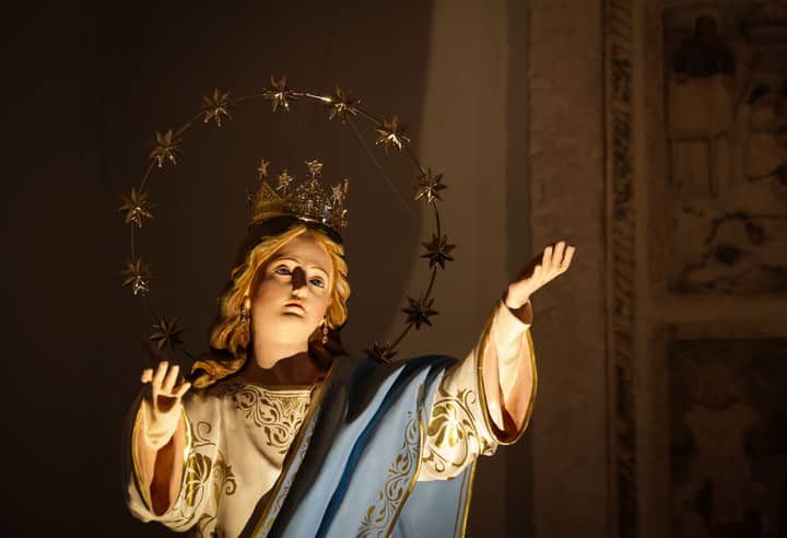Close-up of a decorative religious statue with a starry halo inside a church, emphasized by warm lighting.