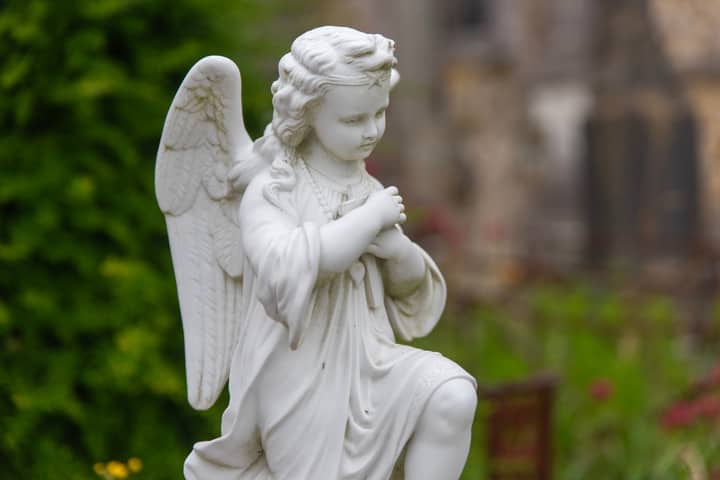 A delicate white angel statue in an outdoor garden, evoking peace and spirituality.