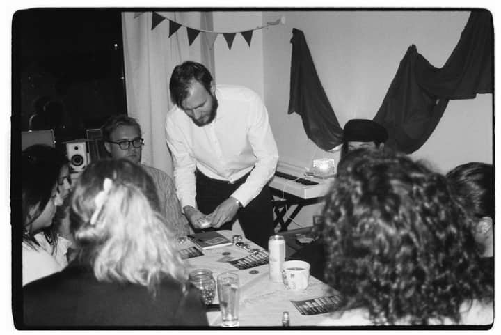 A magician performs card tricks to an engaged group at an indoor party.
