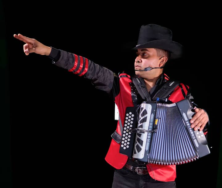 Musician playing accordion with energy, wearing a hat and red jacket.