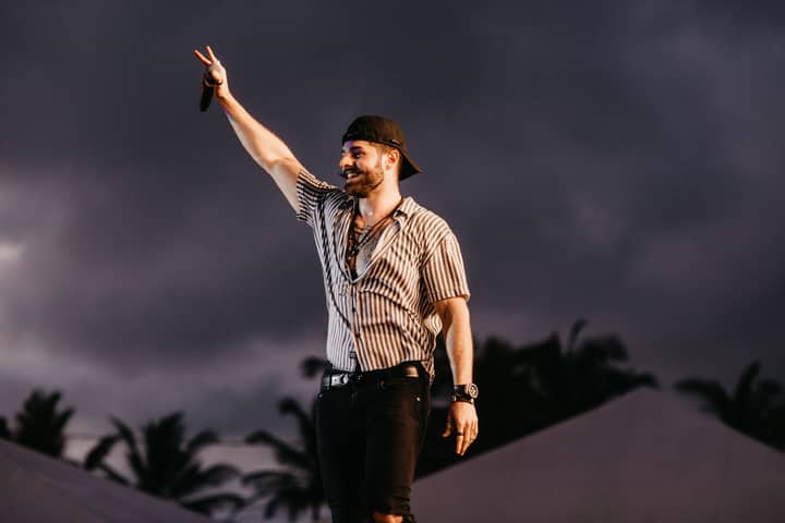 A charismatic man entertains a crowd with a live performance outdoors at sunset.