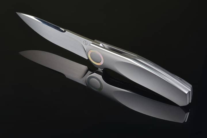 Elegant silver folding knife on a dark reflective background, showcasing modern design and craftsmanship.