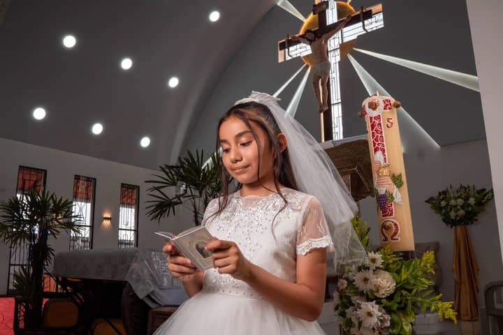 Young girl in white dress reading during communion ceremony in church.