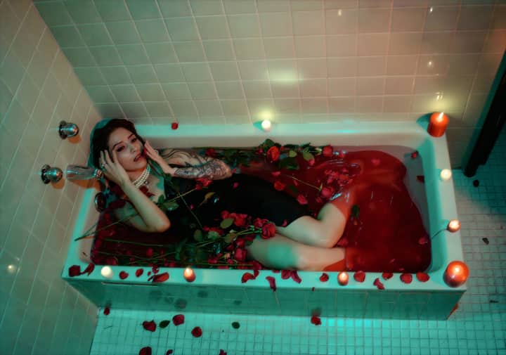 A woman in a red rose-filled bathtub with candlelight ambiance, evoking a serene mood.