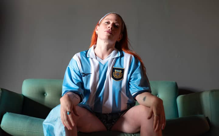Portrait of a person sitting on a couch wearing an Argentinian soccer jersey.