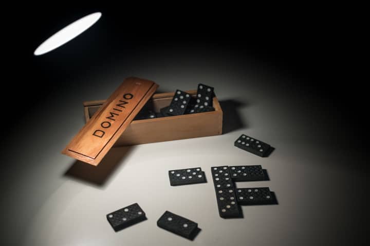 Black domino pieces spilling from a wooden box under dramatic lighting, highlighting a classic game setup.