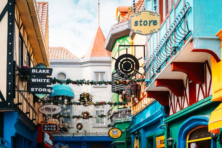A festive shopping street adorned with colorful storefronts and holiday decorations under a bright sky.