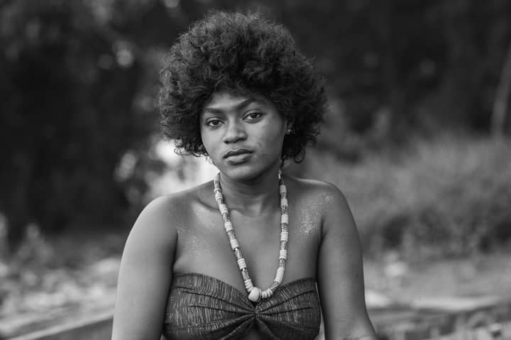 Black and white portrait of a woman with a natural hairstyle and traditional African necklace outdoors.