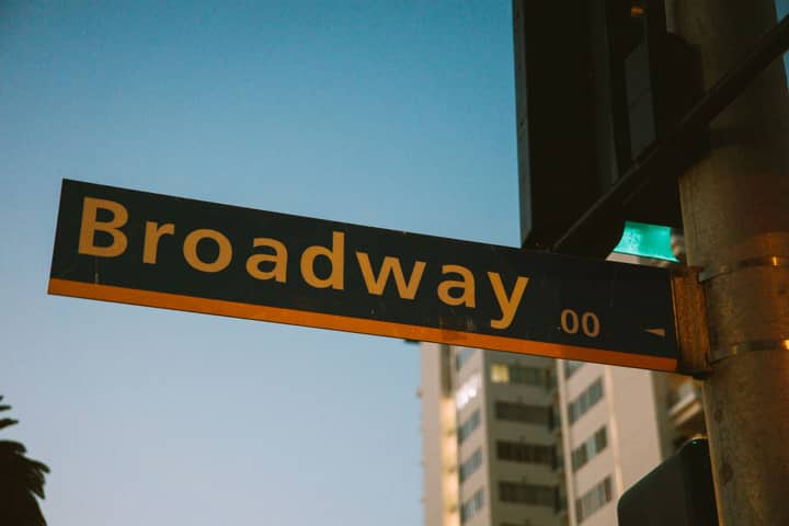 A vibrant street sign depicting Broadway during twilight with a city backdrop.