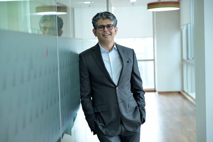 Smiling businessman standing confidently in a modern office hallway, wearing a suit.
