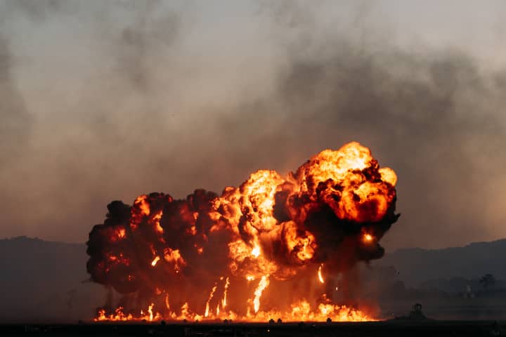 A powerful explosion with intense flames and smoke in an open field during dusk, creating a dramatic scene.