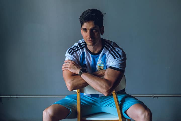 Young man wearing Argentina jersey sitting confidently indoors, showcasing passion for sports.