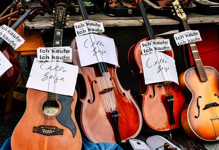 A collection of vintage string instruments on display at an outdoor market with purchase signs.