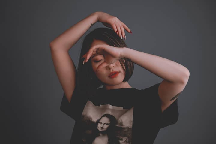 Young reflective ethnic female in stylish t shirt with illustration and red lips standing with closed eyes and raised arms