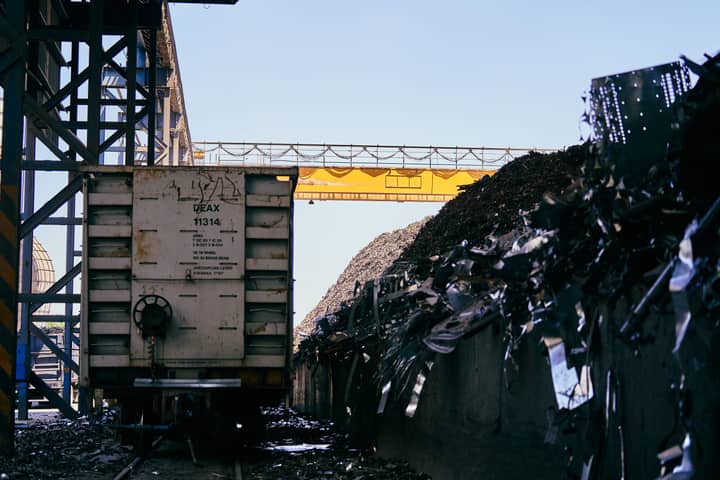 Train car at an industrial scrap metal yard with conveyor belt and metal piles.